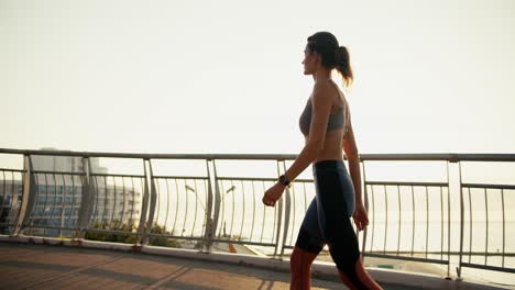 una chica deportiva en un uniforme de verano deportivo camina a lo largo del puente contra el fondo del amanecer