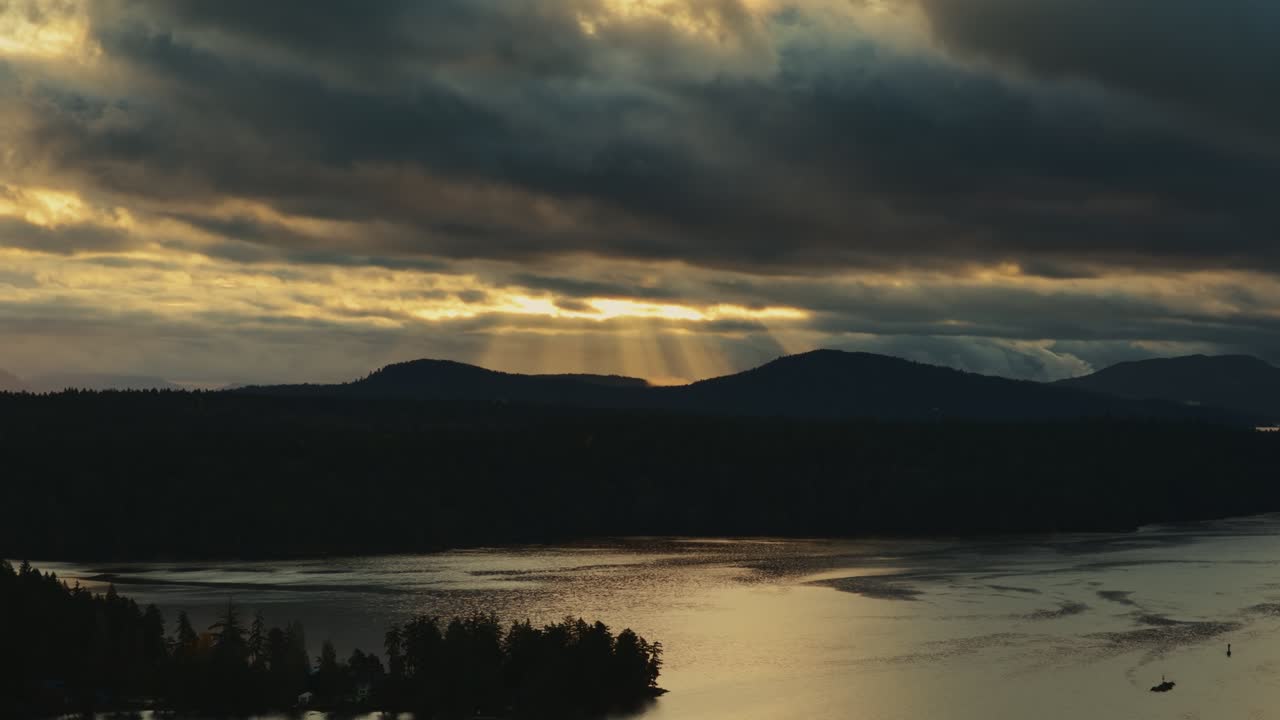 Golden Sunbeams Through Dark Clouds Over Island In Silhouette At Dusk. Gulf Islands Of British Columbia In Canada. wide drone shot