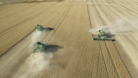 aerial, 3 combine harvesters collecting wheat grains from vast farm field