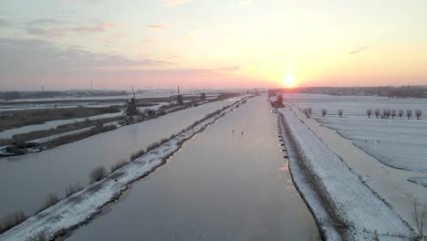 Colorido-Amanecer-En-Kinderdijk,-Sitio-Del-Patrimonio-De-La-Unesco,-Con-Patinaje-Sobre-Hielo-En-Pareja