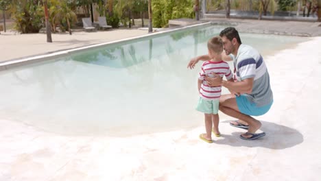 Happy-caucasian-father-and-son-talking-at-swimming-pool-at-beach-house