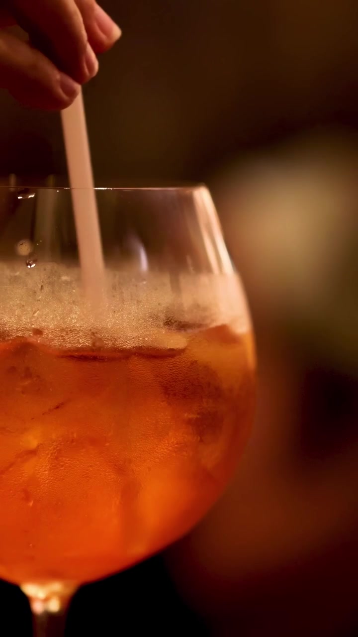 Mano che mescola un cocktail con una cannuccia nel bicchiere
