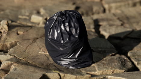 black trash bag lay on a rocky beach