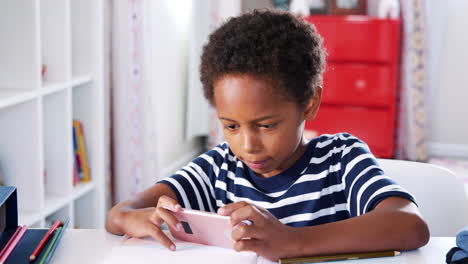 Niño-Sentado-En-El-Escritorio-En-El-Dormitorio-Jugando-En-El-Teléfono-Móvil