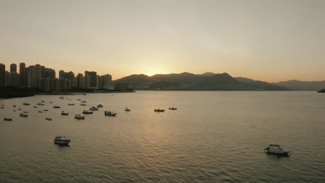 Paisaje-Urbano-Aéreo-De-Hong-Kong-Durante-La-Puesta-De-Sol-Con-Un-Barco-Amarrado-En-La-Bahía-Del-Puerto-Y-El-Paisaje-Urbano-En-El-Fondo