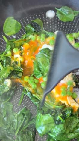 cooking eggs with spinach and peas in a pan