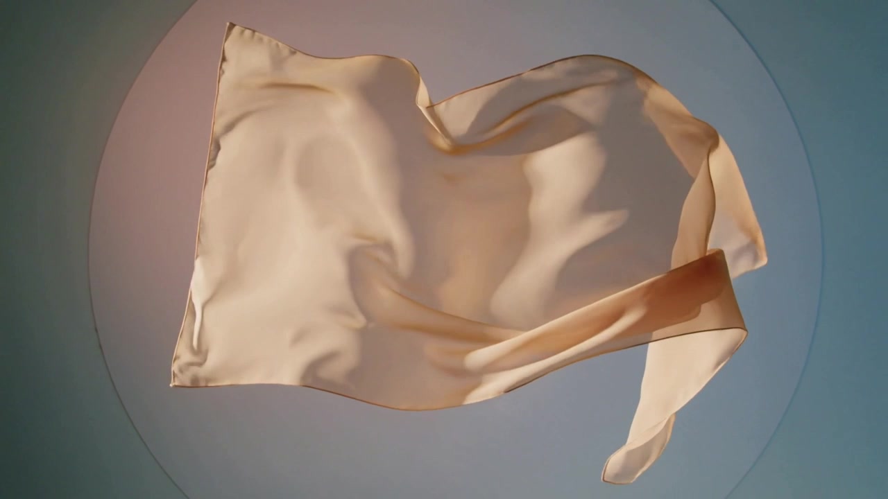 Unfurling peach satin fabric reacting to airflow over studio disc, soft light accenting sheen