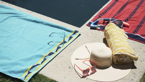 gafas de sol, un sombrero y toallas están al lado de una piscina, sugiriendo un día de ocio