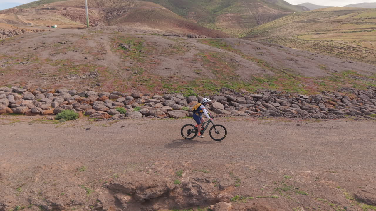 Vista aérea de um ciclista de mountain bike pedalando por uma trilha costeira cênica. O ciclista avança por um caminho de terra com falésias dramáticas e oceano. Gran Canaria, Ilhas Canárias