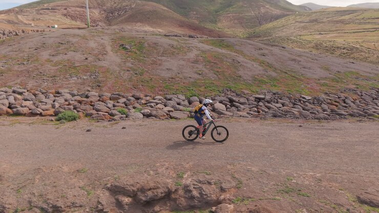 Vista aerea di un ciclista di mountain bike che pedala lungo un sentiero costiero panoramico. Il ciclista si muove su un sentiero sterrato con scogliere mozzafiato e l'oceano. Gran Canaria, Isole Canarie.