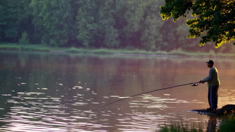 man fishing at sunrise/sunset on a calm lake