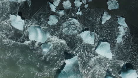 low altitude aerial view of ice pieces on diamond beach, iceland, waves crashing on black sand. part 1.