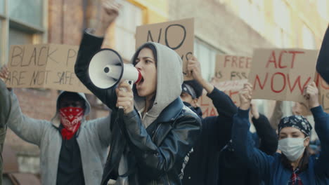 caucasian woman with hoodie and arms up yelling on a loudspeaker in a protest with multiethnic group of people in the street