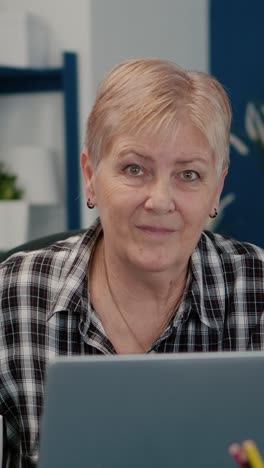 vertical video: old focused woman looking at camera after typing on laptop