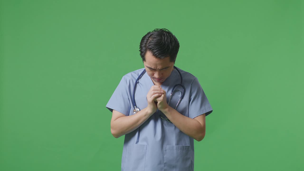 스테토스코프를 들고 있는 아시아 남성 의사는 병원의 녹색 스크린 배경에서 무언가를 위해 기도합니다.