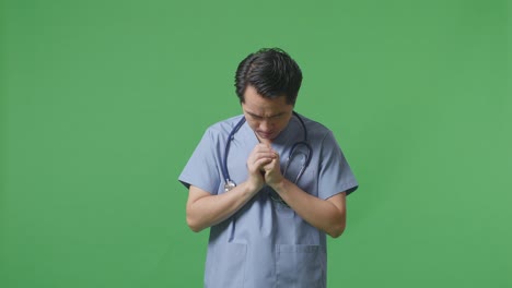 스테토스코프를 들고 있는 아시아 남성 의사는 병원의 녹색 스크린 배경에서 무언가를 위해 기도합니다.