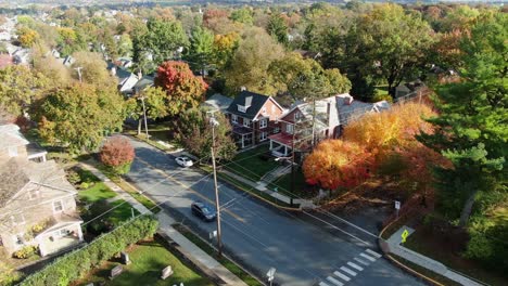 Establishing-shot-of-cars-passing-through-small-town-in-America,-USA-during-autumn-fall-foliage-season