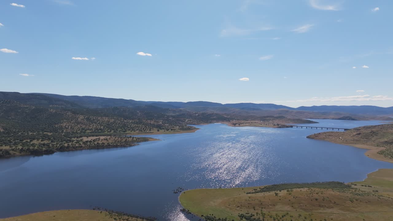 Beautiful frontal drone flight in slow motion over the calm Guadiana River at full capacity during sunset, with blue sky, blue water, and distant blue mountains