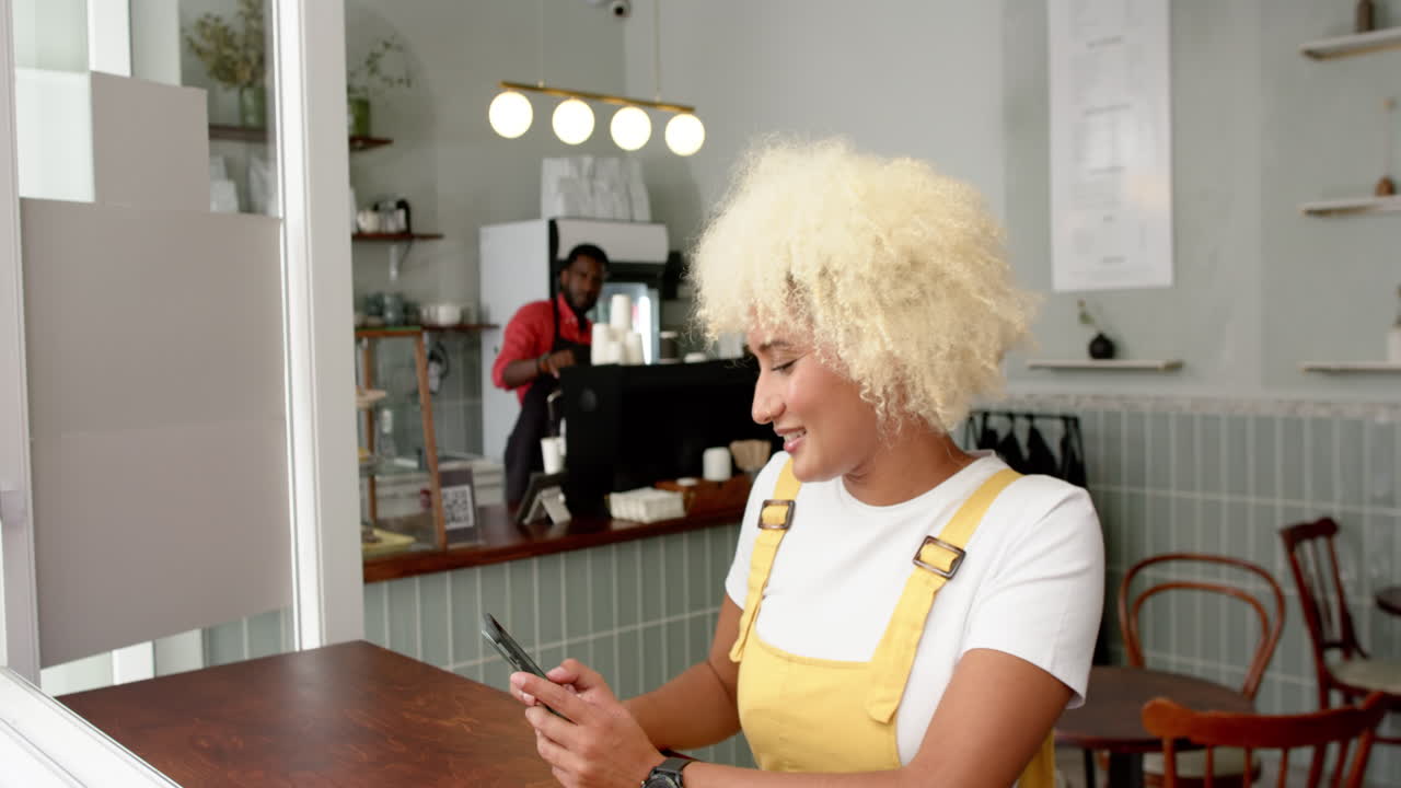 Biracial woman with curly blonde hair uses a smartphone in a cafe