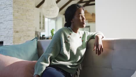 video of thoughtful african american woman sitting on sofa and looking outside window