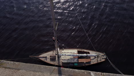 aerial top down static of man balancing on sailboat mast, dark rippled water below, post-storm scene along concrete pier