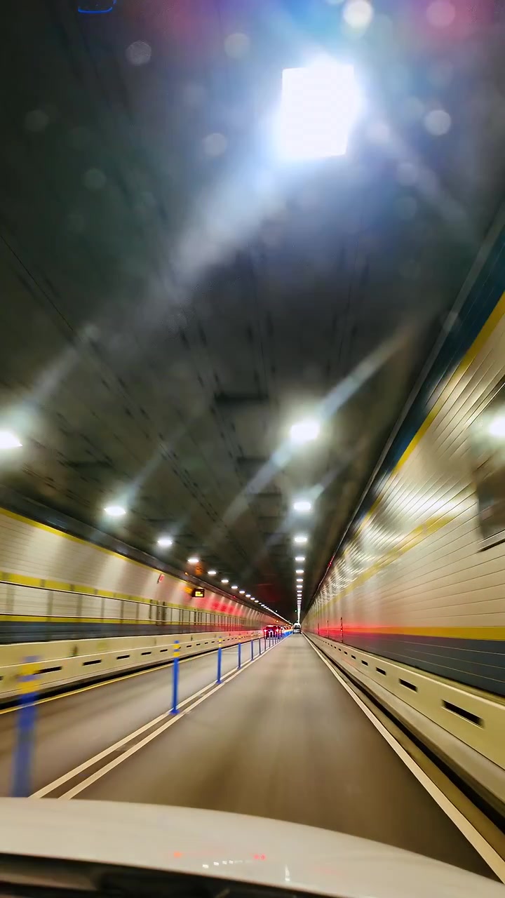 Perspektiivinen ajonäkymä valaistun tunnelin läpi liikesumennuksella. Maantietunnelin sisätilat valkoisilla kaakeliseinillä ja keltaisilla yksityiskohdilla, näyttäen valojuovia ajoneuvojen liikkeestä.