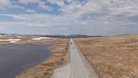 semi-trailer trucks and cars driving in the road along the lake in hardangervidda plateau in norway. - aerial shot