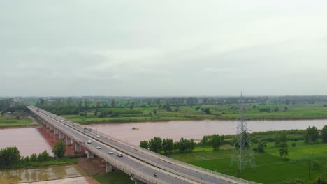 Vista-Aérea-Del-Paso-Elevado-Sobre-Tierras-Agrícolas-Cerca-Del-Río,-Y-El-Canal-Después-De-La-Lluvia-Con-Agua-Turbia-Lluviosa-Fuera-De-La-Ciudad-En-La-Región-De-Punjab,-India