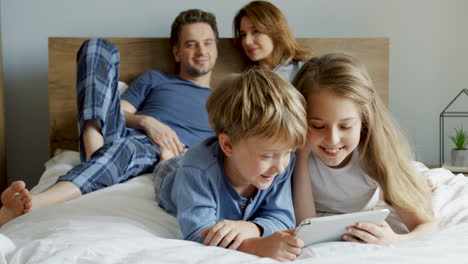 Close-up-view-of-a-little-girl-and-her-brother-lying-on-the-bed-and-watching-something-on-the-tablet