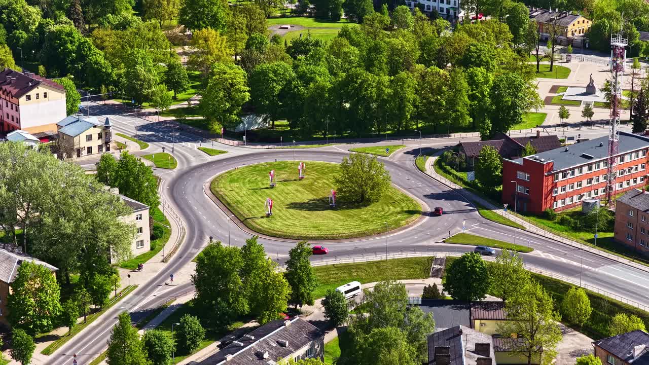 Cinematic bird's-eye view of traffic moving through a green circular intersection in town
