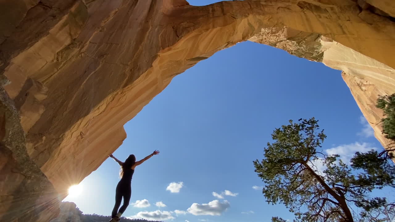 mujer joven bajo el majestuoso arco natural levantando los brazos