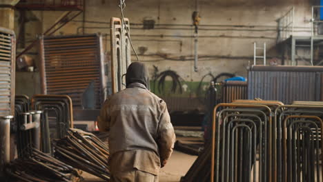 laborer in uniform carries metal frame of pipes in workshop