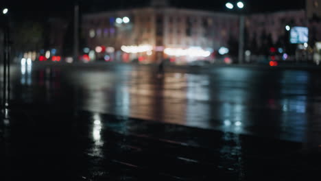 blurred view of cars passing on a city road at night with vibrant light reflections on the wet pavement
