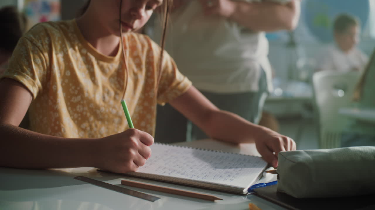 Muslim Primary School Girl Wearing Hijab Sitting at the Desk Writing School Test in Notebook
