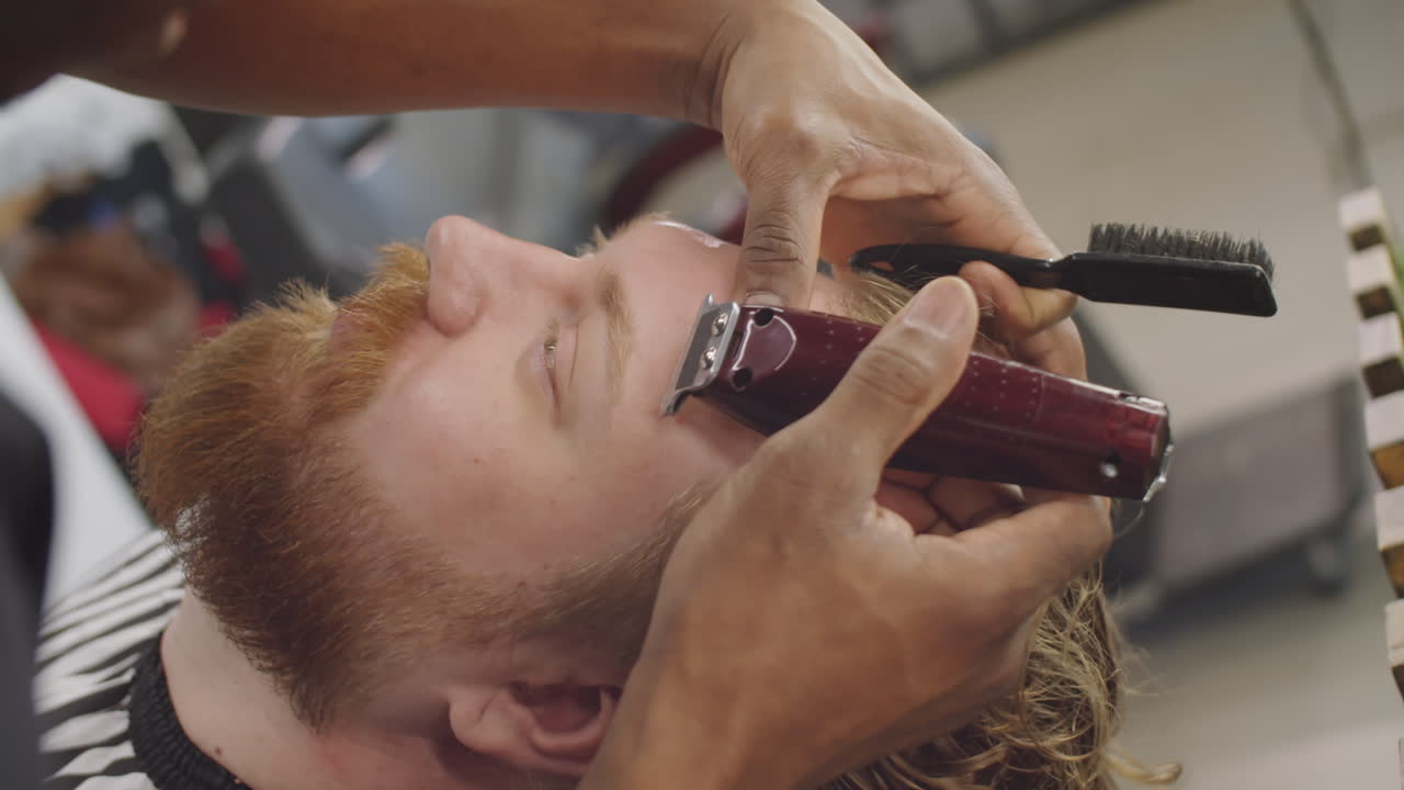 barbero afeitando el cabello en la frente del hombre con un cortador