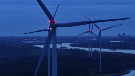 rotating wind turbines next to river oude maas at dusk - aerial drone shot