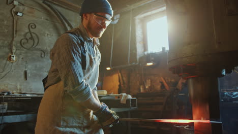 blacksmith forging iron rod with hydraulic press machine in workshop