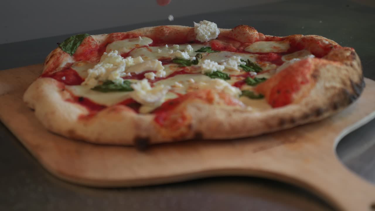 Mezzo primo piano delle mani di uno chef che aggiunge ricotta a una pizza cotta in una cucina all'aperto