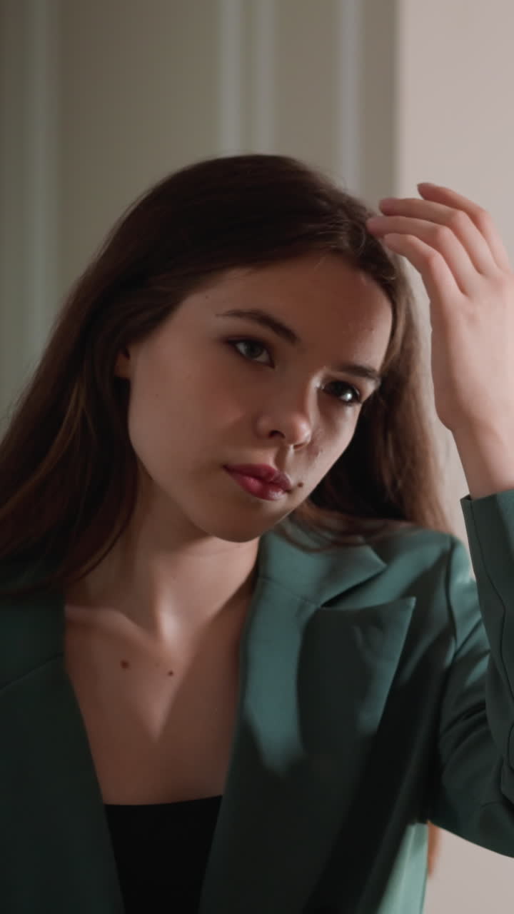 진지한 여자가 거울 앞에서 머리카락을 조정합니다. 자신감이 없는 여자가 드레싱 테이블을 완벽하게 바라보는 데 집중합니다. 불안한 젊은 여자가 아름다움 루틴을합니다.