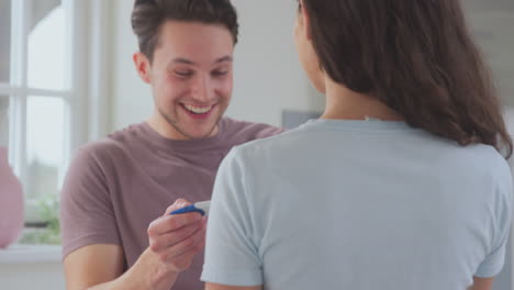 Pareja-Transgénero-En-Casa-En-La-Cocina-Con-Una-Mujer-Hombre-Sorprendente-Con-Prueba-De-Embarazo-Positiva