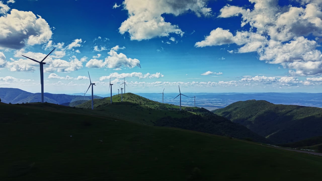 昼間の田園風景、青空と雲の下、丘に立つ風力発電の風車。