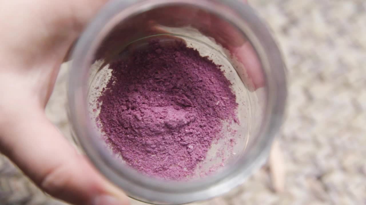 Close up shot of hand holding glass container with pigment powders collected from the extraction of flower petals.