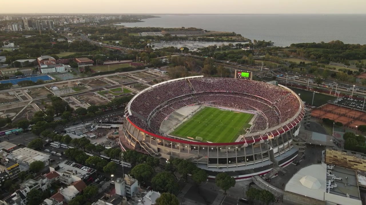 Vista aérea del Estadio Monumental en Buenos Aires durante un partido, con el estadio lleno y el océano de fondo