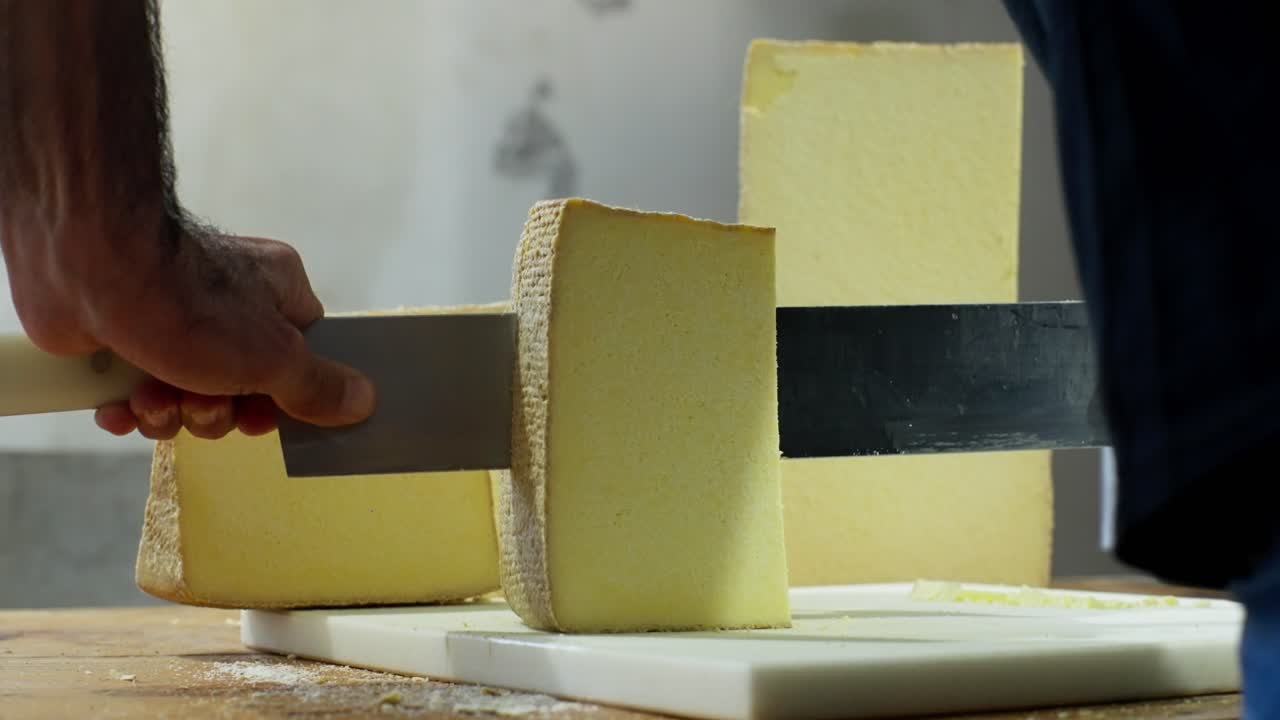 A cheesemaker slices large blocks of cheese with a sharp knife on a cutting board