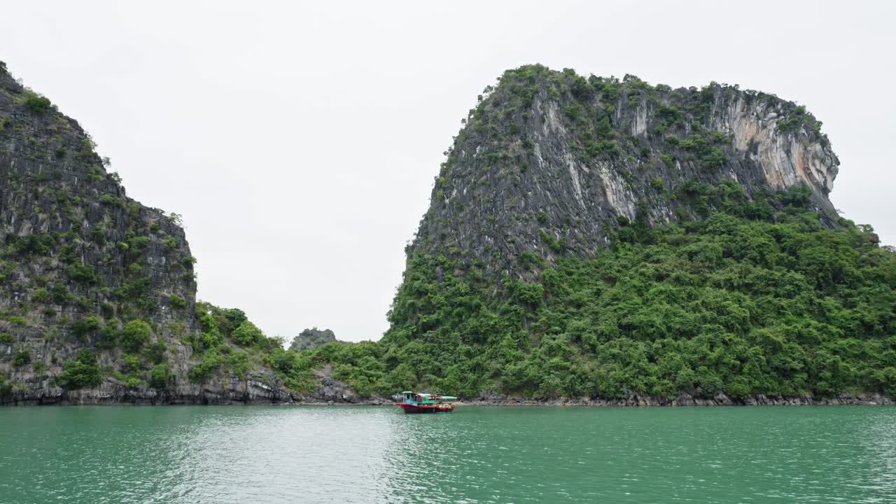 베트남의 석회암 숲 산맥을 배경으로 하롱 만에서 항해하는 전통적인 보트