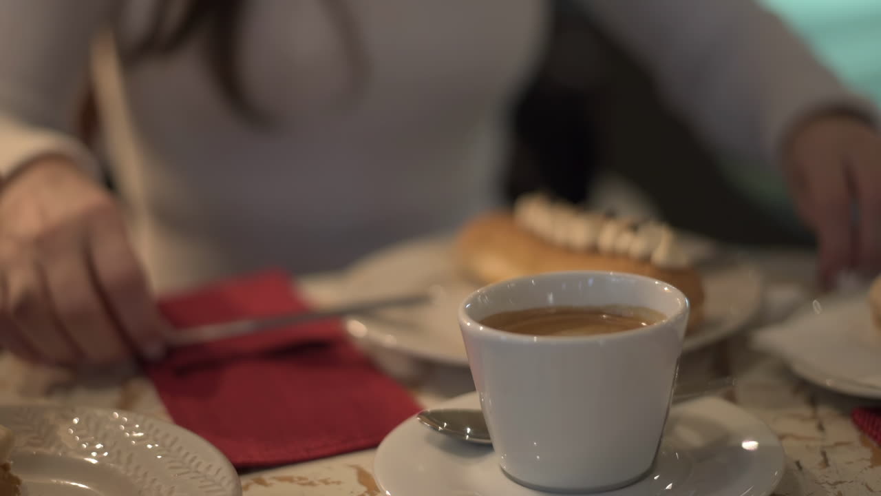Close up of coffee on a table with a woman eating an eclair on the background