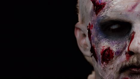 zombie man face makeup with wounds scars and white contact lenses looking at camera, trying to scare