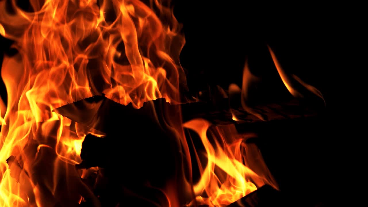 Movimento dettagliato di un bellissimo falò che arde vivacemente su sfondo nero. Ceppi che bruciano nel falò con una fiamma arancione. Primo piano
