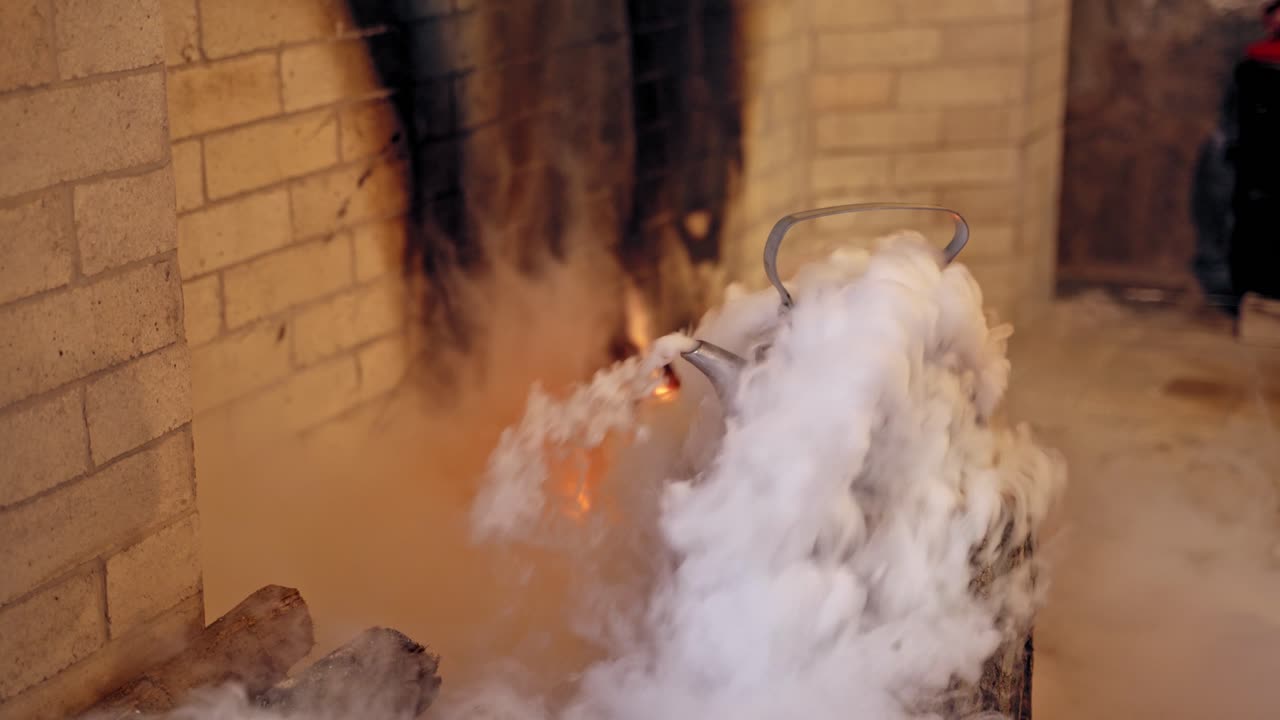 White steam coming from the kettle on a wooden log indoors. Boiling kettle near the fireplace. Santa's hand taking kettle with hot water.