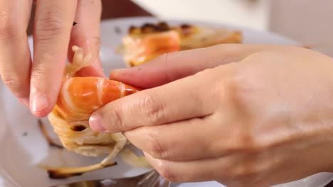 close-up of hands delicately peeling shrimp, showcasing precision and technique on a white plate.